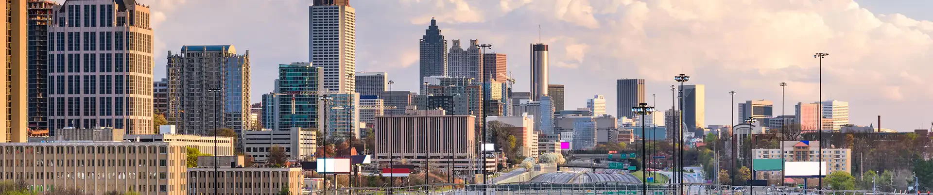 Aerial view of Atlanta's skyline with skyscrapers, highways, and greenery under a blue sky with fluffy clouds.