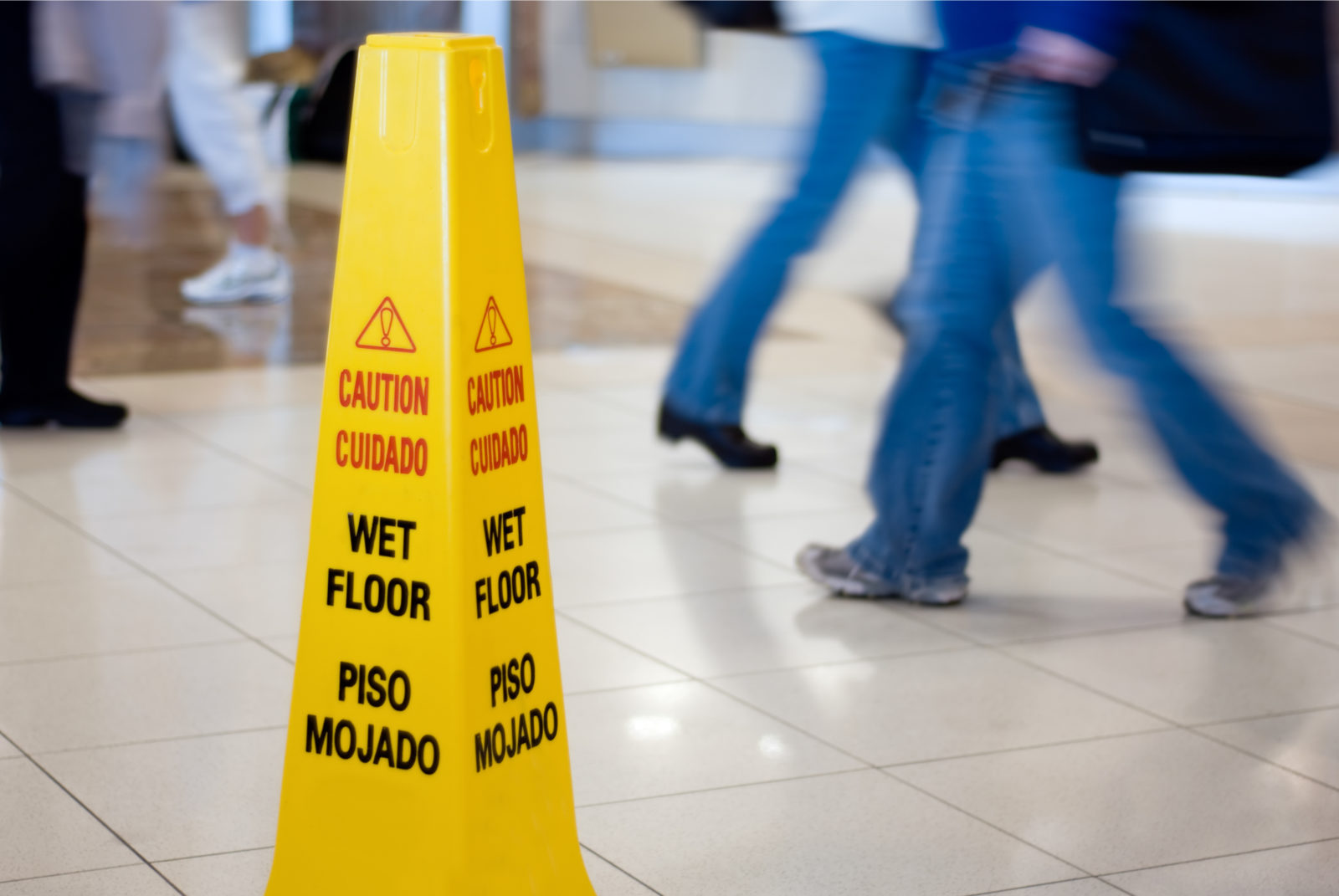 Caution Wet Floor sign with people walking in the background. Understanding Slip and Fall Accidents and Negligence Law Suits in Georgia.